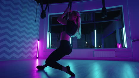 A-woman-does-yoga-and-stretching-on-a-hanging-hammock-in-neon-light.-A-woman-is-flying-in-a-hammock-in-the-studio-doing-stretching-and-body-exercises.-Exercises-in-the-air